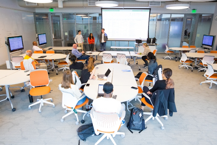 Three students address a group of students inside a Bloch Executive Hall classroom